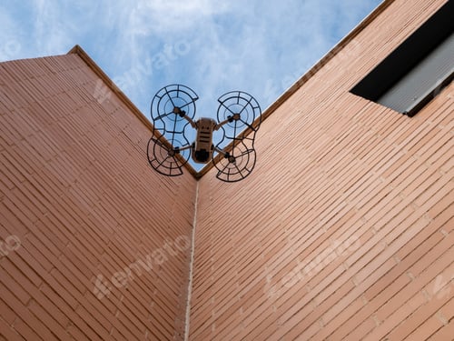 Preview: Worm's eye view of a drone with propeller guard flying beside a building