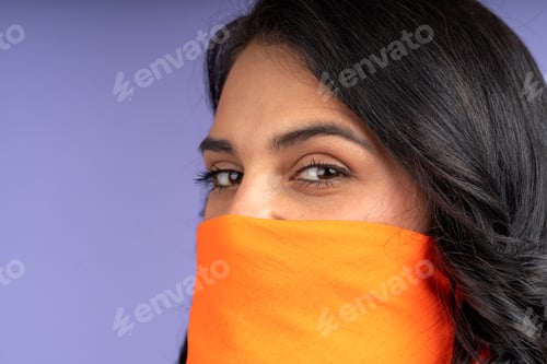 Preview: Woman covering her face with orange scarf on purple background
