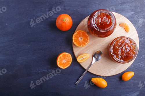 Preview: Tangerine and kumquat jam in a glass jar on a black wooden background.