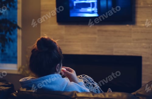 Preview: Young teenage girl is sitting on a couch watching TV and eating popcorn