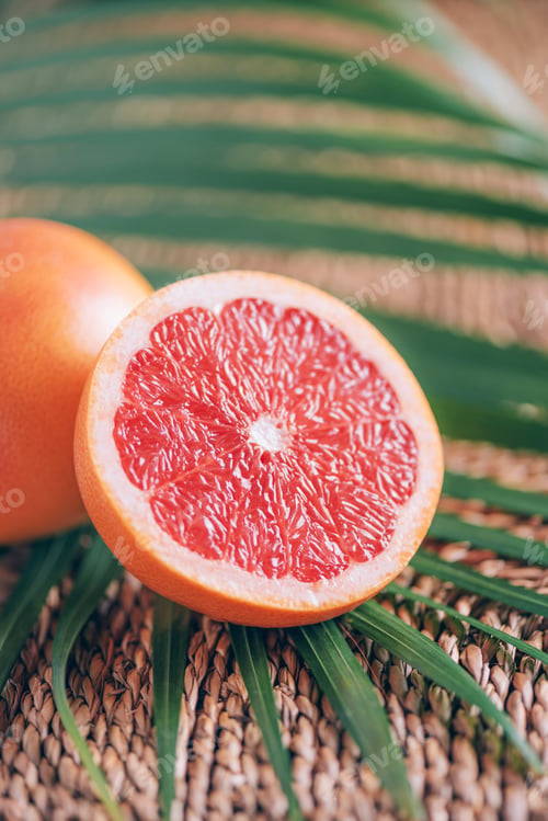 Preview: Fresh red grapefruit with palm leaves on rattan background. Copy space. Creative design banner