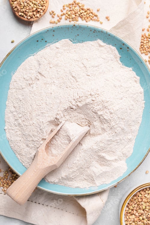 Preview: Buckwheat flour in a blu ceramic plate, raw green buckwheat grain on a bowl on light background