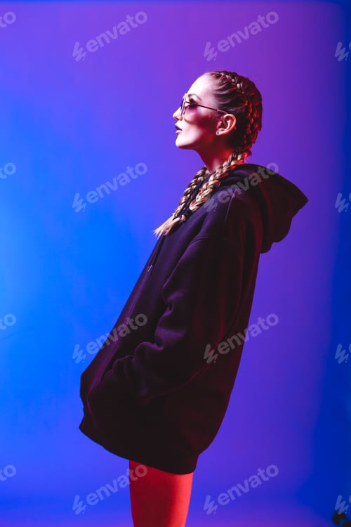 Preview: Portrait of fashion girl in a black sweater with a hood and sunglasses round shape in neon light in