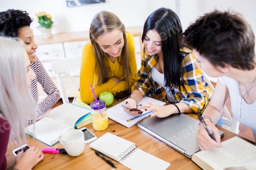 Preview: Group of female students sharing cell phone at table at home