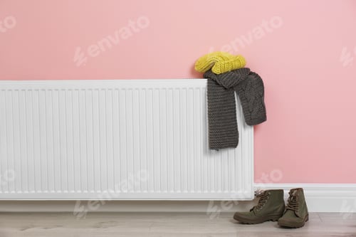 Preview: Heating radiator with knitted cap, scarf and shoes near color wall