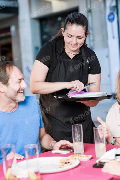 Preview: latin waitress woman smiling serving food in restaurant to a mature group of friends together.