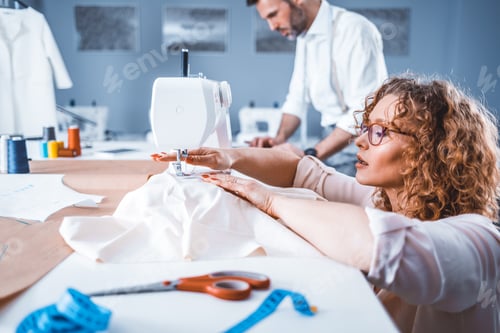 Preview: Professional tailors during work on project in fashion design studio, using sewing equipment