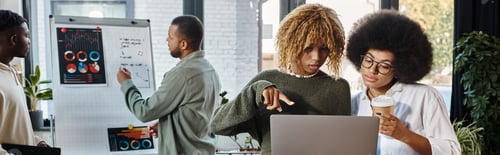 Preview: two women looking at laptop while their friends working on graphs on backdrop, business, banner