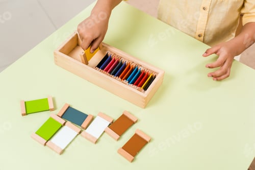Preview: Cropped view of kid playing educational game with colorful boards at table in montessori school