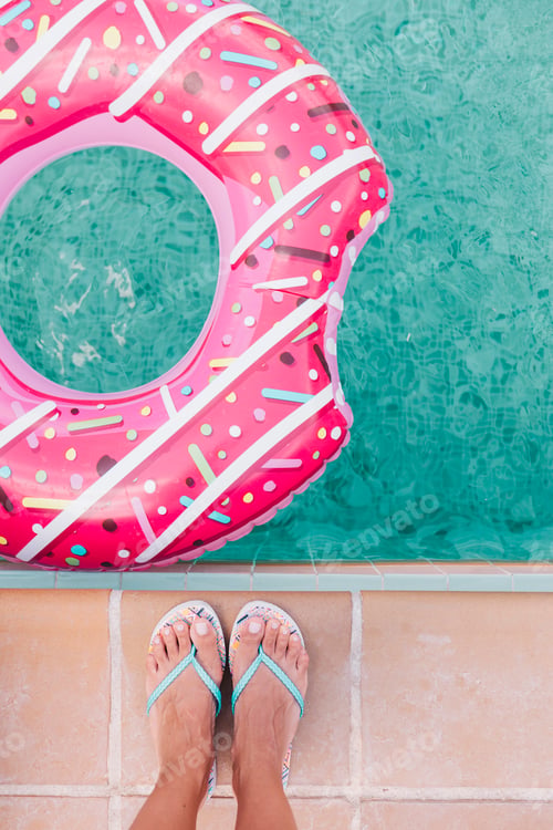 Preview: top view of a woman feet flat lay. Woman relaxing in the pool with pink donuts in hot sunny day