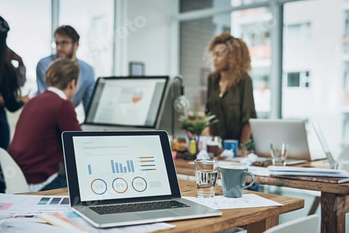 Preview: Closeup shot of a laptop with graphs on the screen and a team working in the background