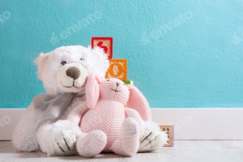Preview: Teddy bear and knitted bunny relaxing with wooden blocks in playroom