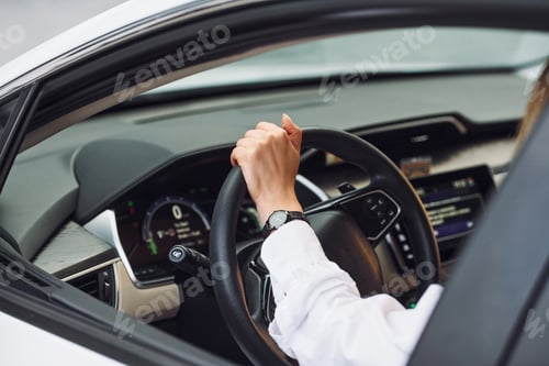 Preview: Sitting and driving. Young woman in white clothes is with her electric car at daytime