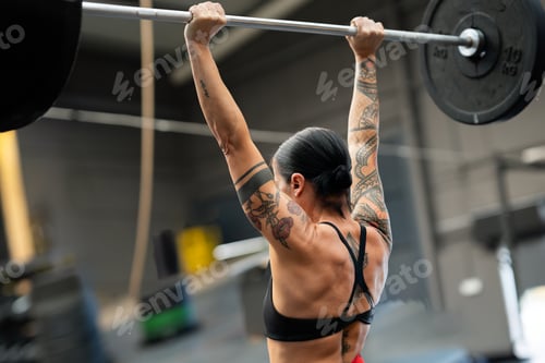 Preview: Rear view of a strong fit woman lifting barbell