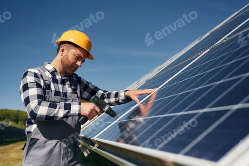 Preview: installation by using drill. Engineer with photovoltaic solar panels outdoors at daytime