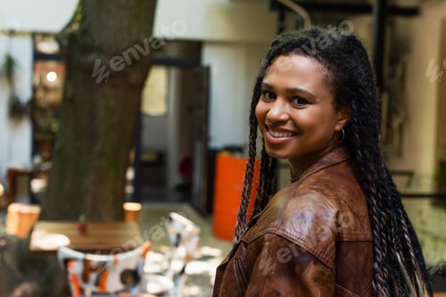 Preview: joyful african american woman in brown leather jacket smiling outside