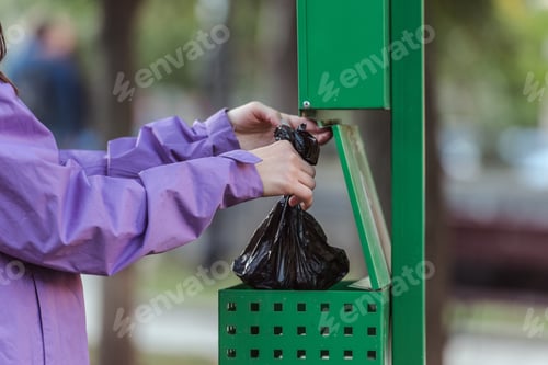 Preview: cropped shot of woman putting bag in trash can in park, cleaning after pet concept