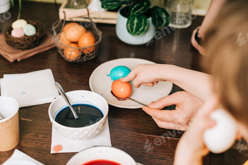 Preview: Easter day. Male Father and son painting eggs on wooden background. Family sitting in a kitchen