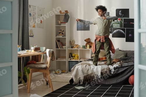 Preview: African American schoolboy standing on double bed and exercising