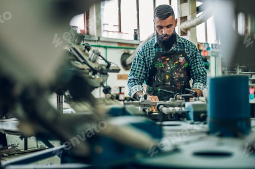 Preview: Male worker pressing ink on frame while using the printing machine in a workshop