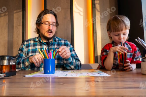 Preview: Portrait of child with his father drawing with pencils in cafe