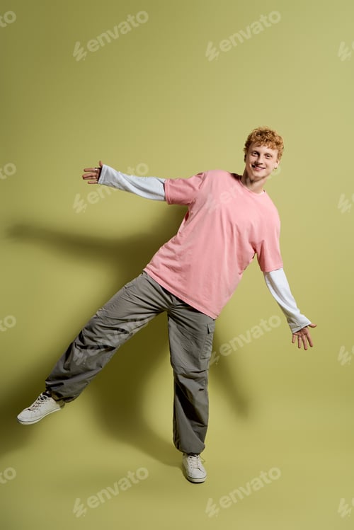Preview: Stylish young man poses playfully against a soft green backdrop in trendy casual attire