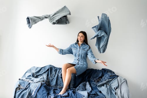 Preview: Fashion designer sitting on denim couch throwing clothes in air