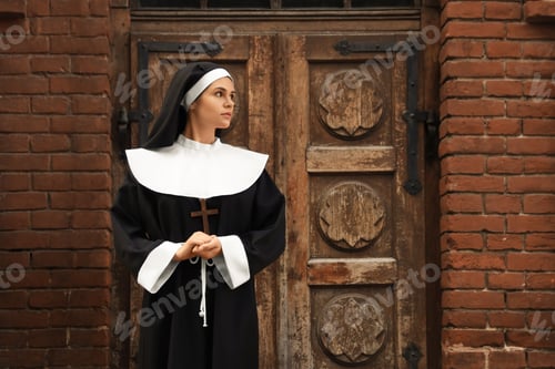 Preview: Young nun with Christian cross near old building outdoors