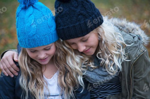 Preview: Blond haired sisters wearing knit hats looking down in garden
