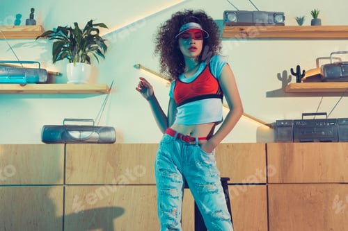 Preview: portrait of young fashionable woman in cap and jeans with hand in pocket looking away