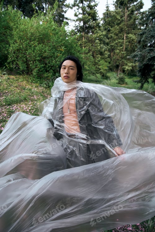 Preview: Stylish young man enjoying a serene moment in a park with flowing plastic