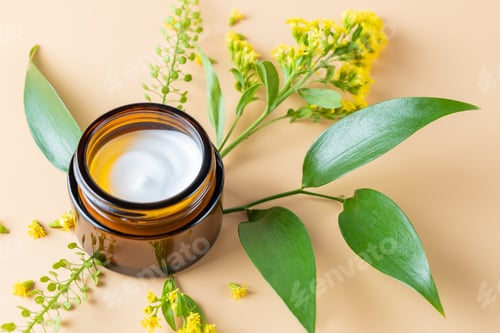Preview: Dark glass Jar with face cream and spring flower on a beige background. Unbranded cosmetics packagin