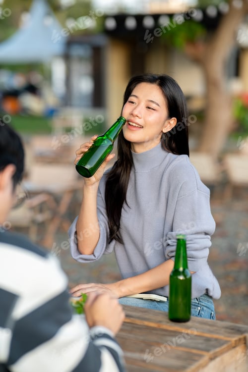 Preview: Pretty asian woman holding drink bottle across man friend sitting at table in campground restaurant.