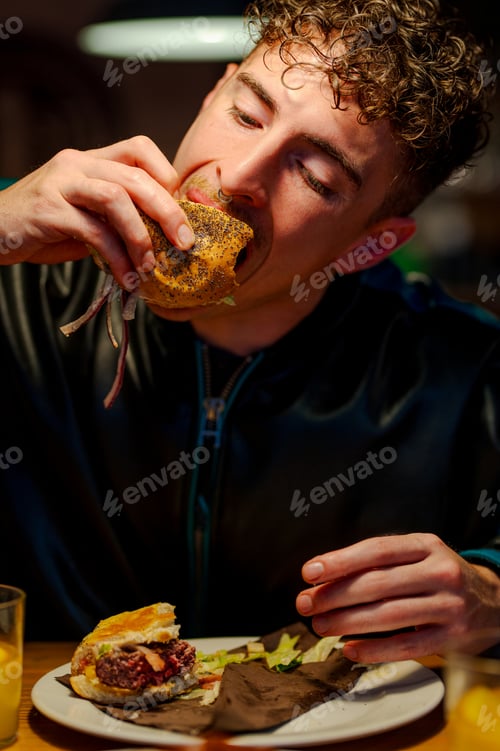 Preview: Young man eating burger in hamburger restaurant