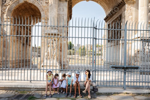 Preview: Mother with five kids tourists sitting under spectacular Arch of Constantine, Rome, Italy.
