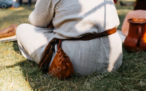 Preview: Person in medieval rustic clothing with a leather pouch on his belt resting sitting