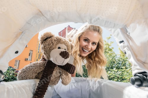 Preview: smiling beautiful mother holding teddy bear in baby stroller