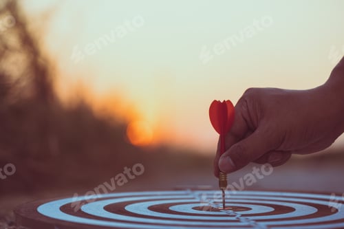 Preview: Close up hand hitting red arrow to target dartboard at sunset background. Business targeting