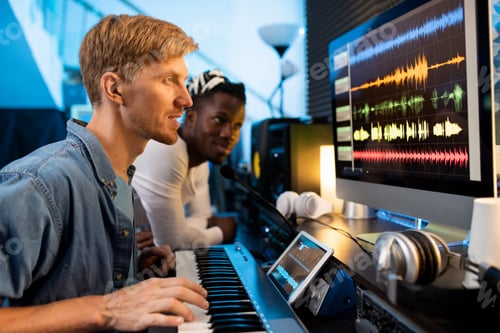 Preview: Young man with pianoboard looking at computer screen during work in studio
