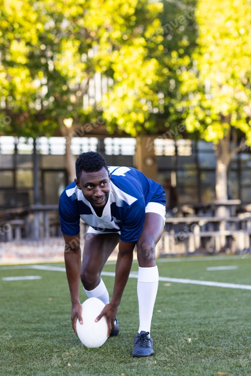 Preview: African American young male athlete wearing sportswear, stretching on field
