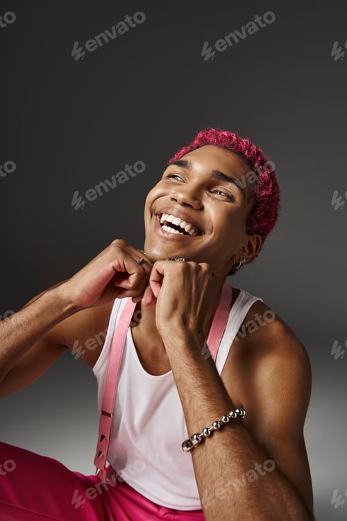Preview: handsome stylish man with pink hair holding hands under chin and smiling sincerely, fashion concept