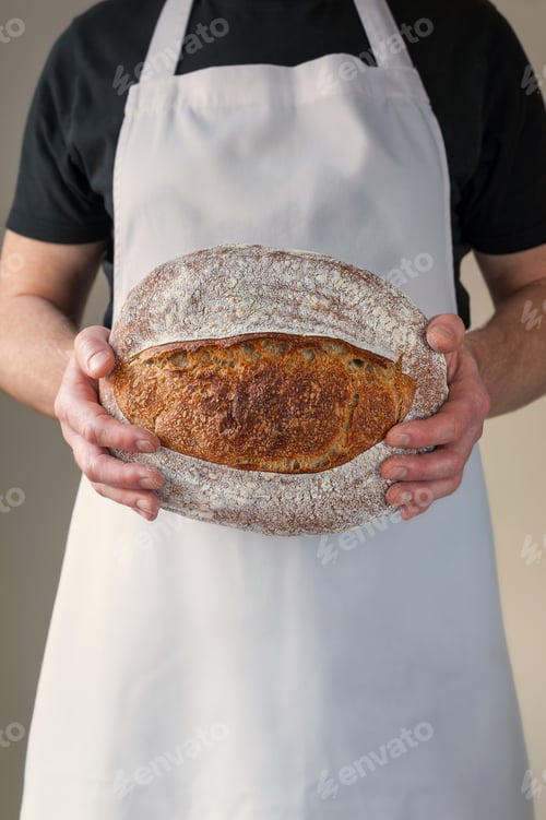 Preview: Close-up at bakers hands holding a loaf of bread in front of him.