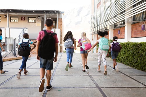 Preview: Rear view of group of diverse students with backpacks running at elementary school