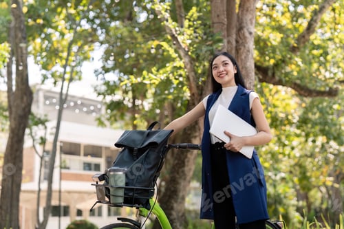 Preview: Asian businesswoman with bicycle holding a laptop and outside the office building. Woman commuting