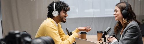 Preview: side view of happy indian man in headphones and yellow jumper gesturing and talking to smiling