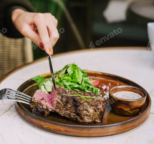 Preview: female hands in a restaurant at the table cut beef striploin steak