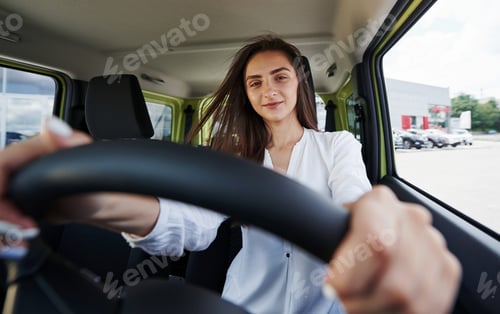 Preview: Happy owner. Front view of woman that drives modern new car in the city