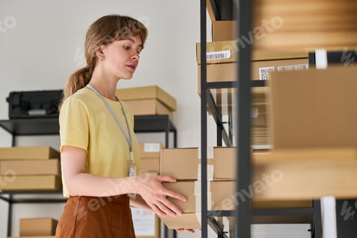 Preview: Young woman in yellow blouse putting boxes on rack in warehouse