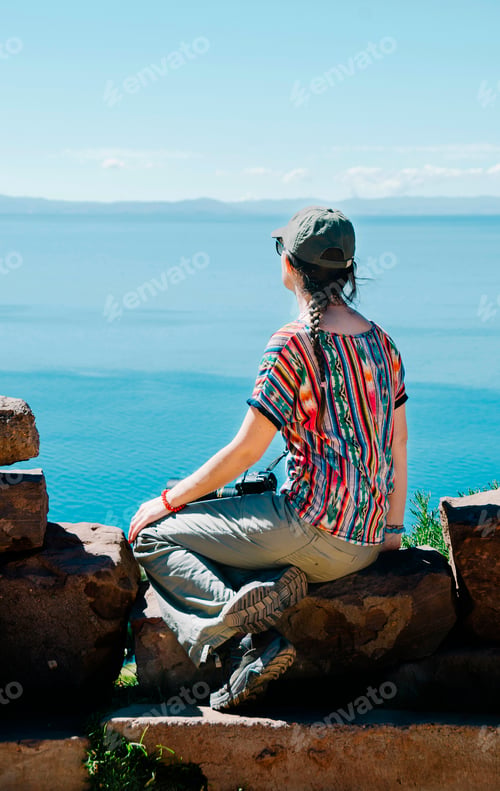 Preview: Peru, Taquile, back view of woman sitting on a rock enjoying view over Titicaca lake