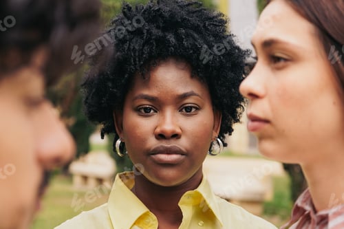 Preview: African woman face betweern blurred peple looking to the camera with serious expression.